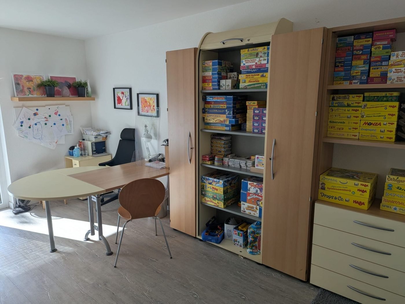 Therapieraum mit Arbeitstisch und Schränken voller Lern- und Therapiespiele
